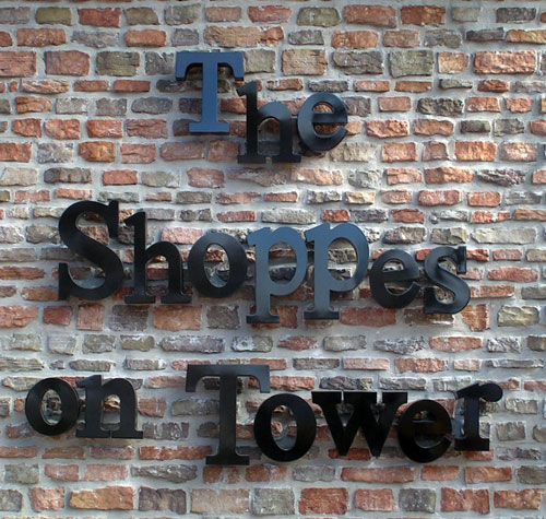 Photo of the front signage for The Shoppes on Tower featuring black letters on a brick wall